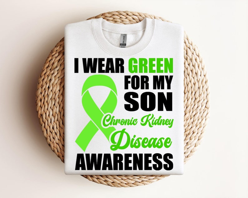 May include: White t-shirt with a green ribbon and the text "I wear green for my son Chronic Kidney Disease Awareness".