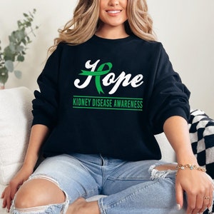 May include: Black sweatshirt with a green ribbon and the word "Hope" in white lettering. The text "Kidney Disease Awareness" is printed below the word "Hope".