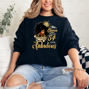 May include: Black sweatshirt with gold glitter text that reads "This Queen Makes 54 Look Fabulous". The text is surrounded by a gold glitter crown and a black and gold illustration of a woman's face.