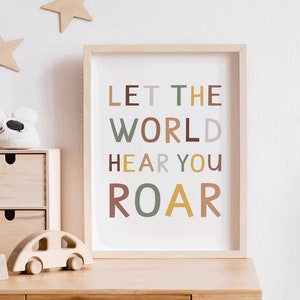 Pode incluir: Uma impressão emoldurada com o texto "LET THE WORLD HEAR YOU ROAR" em letras coloridas sobre um fundo branco. As letras estão em diferentes tons de marrom, verde e amarelo.