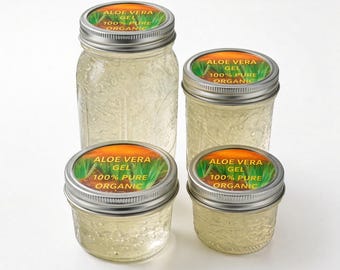 May include: Four clear glass jars of varying heights filled with translucent aloe vera gel. Each jar features a silver metal lid with a circular label reading ALOE VERA GEL 100% PURE ORGANIC over a green plant and orange sunset background.
