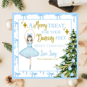 May include: A square Christmas card with a watercolor illustration of a ballerina in a blue tutu and a Christmas tree. The card reads "A Merry Treat for Your Dancing Feet" and "Merry Christmas Love, Lucy."