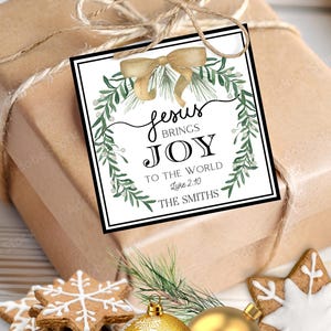 以下が含まれることがあります： 茶色の紙で包まれたクリスマスプレゼント。 「イエスは喜びをもたらす」と書かれたタグが付いています。 タグには金の弓と緑の葉が描かれています。 お祝いのオーナメントとジンジャーブレッドクッキーも含まれています。