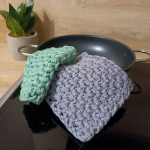 Peut inclure: Deux maniques en crochet, l'une verte et l'autre grise, sont posées sur une surface noire. La manique verte est pliée sur la manique grise.
