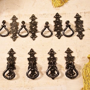 Può includere: Dieci tiretti per cassetti in metallo nero con disegni decorativi. Ogni tiretto ha una maniglia ad anello e una piastra posteriore decorativa.