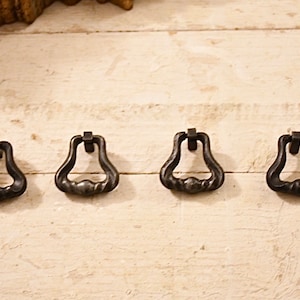 Könnte beinhalten: Vier schwarze Metall-Schubladengriffe in Glockenform mit einem gedrehten Design.