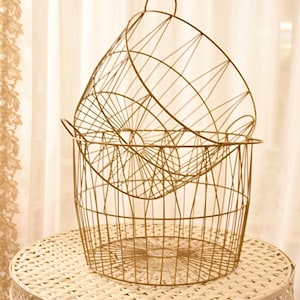 May include: Two gold wire baskets stacked on top of each other on a white table with a woven top.