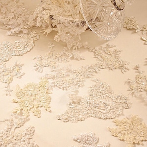 May include: Assortment of white lace appliques with pearl and sequin embellishments. The appliques are arranged on a white surface.