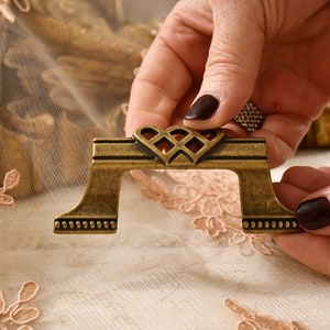 May include: A gold-toned metal drawer pull with a decorative heart-shaped design. The pull has a smooth, polished finish and a slightly raised edge.