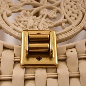 Può includere: Un chiavistello a rullo in metallo dorato con due rulli. Il chiavistello è montato su una superficie bianca.