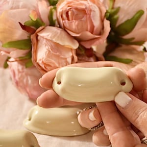 Peut inclure: Cinq poignées de tiroir en céramique blanc cassé avec une forme arrondie et incurvée. Les poignées ont deux trous pour le montage.