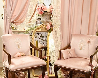 May include: Two antique pink velvet armchairs with dark wood frames. Each chair has an embroidered design on the back and is adorned with pearls and flowers. The background features pink curtains, lace curtains, and a gold mirror, creating a romantic, vintage aesthetic.