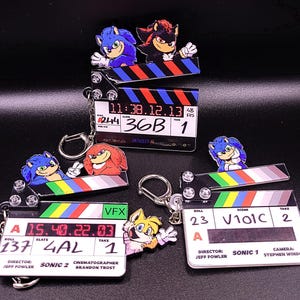 May include: Keychains featuring characters from the Sonic the Hedgehog franchise. Each keychain has a character image on a film clapperboard. The clapperboards have text including "Sonic 2" and "Sonic 1".
