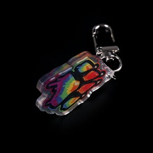Photograph of an acrylic keychain with a pride flag paw print design on a black surface standing on it's side. Side not covered in starry holographic coating is facing forwards and towards the camera
