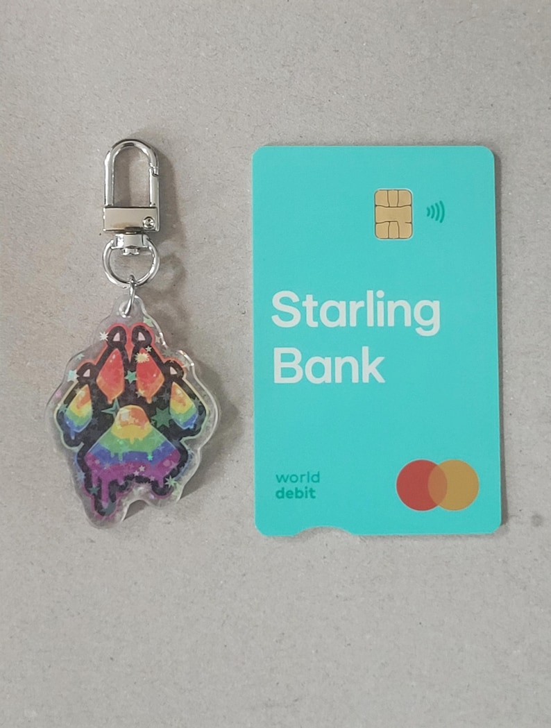Size comparison of a Pride Paw Flag Keychain by Kaladania. Keychain is compared to the size of a standard credit card (of which - including the height of the hook - the keychain is as tall as the credit card).