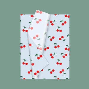 May include: A sheet of light blue wrapping paper featuring a repeating pattern of bright red cherries with green stems and leaves. The paper is folded over at the top, revealing a white underside that also displays the same cherry pattern.