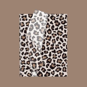 May include: Leopard print wrapping paper with a sheet partially peeled back, revealing the same pattern. The design features a cream background with brown and black spots. The paper is rectangular and set against a brown backdrop.