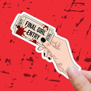 May include: A sticker featuring the words "FINAL GIRL ENTRY" in black, with a blood splatter design. The sticker is held by a hand with black nail polish against a red background.