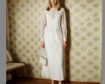 Puede incluir: Un vestido maxi blanco con una superposición transparente y un escote en V. El vestido tiene dos bolsillos en la parte delantera y se estiliza con un bolso blanco y tacones blancos.