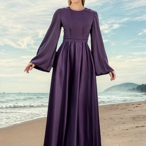 May include: A woman wearing a long, flowing purple dress with long sleeves and a fitted waist. The dress has a simple, elegant design and is perfect for a special occasion.