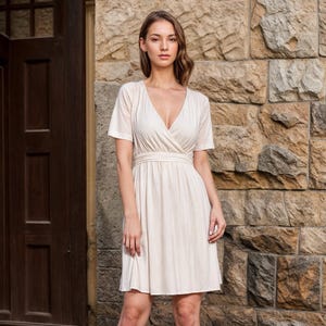 May include: A white wrap dress with short sleeves and a V-neckline. The dress has a fitted bodice and a flowy skirt.