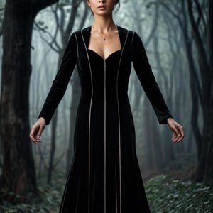 Puede incluir: Una mujer con un vestido de terciopelo negro y un sombrero de bruja negro puntiagudo. El vestido tiene una cremallera en la parte delantera y está adornado con líneas verticales. Está de pie en un entorno de bosque oscuro.