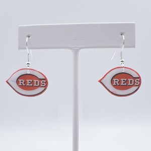 May include: A pair of silver dangle earrings with red and white Cincinnati Reds logo charms.