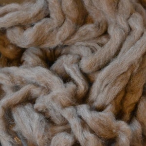 May include: A close-up of a pile of light brown and gray alpaca fiber. The fiber is soft and fluffy, and it is perfect for spinning or felting.