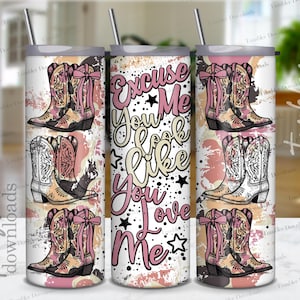 May include: A white tumbler with a pink and white design featuring cowboy boots and the text "Excuse Me You Look Like You Love Me".