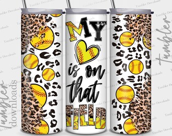 Puede incluir: Un vaso blanco con un diseño de estampado de leopardo y gráficos de softbol. El texto "My heart is on that field" está impreso en negro en el vaso.