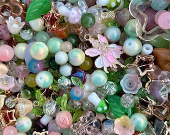 May include: A collection of colorful beads and charms in various shapes and sizes. Includes pink, green, and clear beads, along with star, flower, and mushroom charms. A pink fairy charm is also present, creating a whimsical aesthetic.