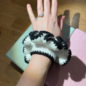 May include: A white and black crocheted hair scrunchie with a ruffled edge.