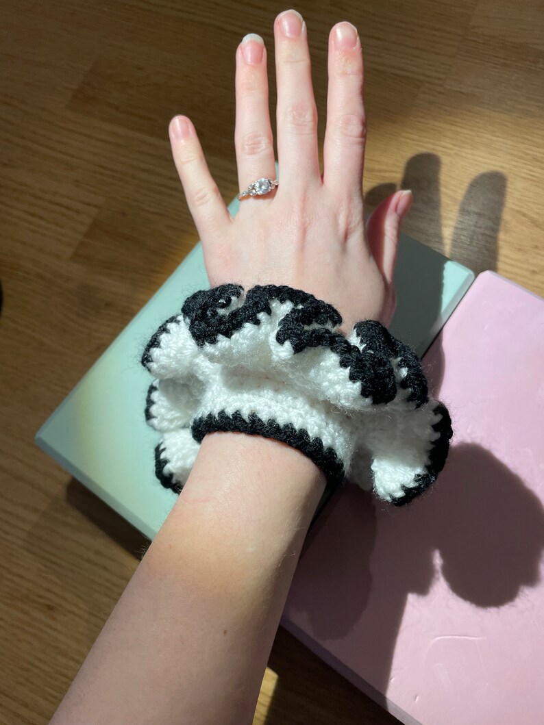 May include: A white and black crocheted hair scrunchie with a ruffled edge.