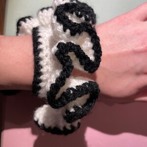 May include: White crocheted hair scrunchie with black trim. The scrunchie is gathered in a ruffled style.