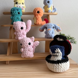 May include: A collection of crocheted Pokemon characters, including Pikachu, Squirtle, Bulbasaur, Charmander, and Jigglypuff. The characters are displayed on a wooden shelf.