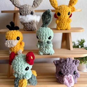 May include: A collection of handmade crochet plush toys in various colors. The toys include a yellow Pikachu, a gray bunny with a white chest, a green turtle with a red flower, and other characters. Each toy has black eyes.