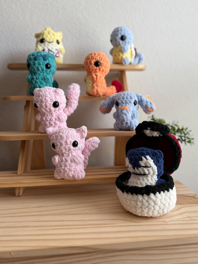 May include: A selection of colourful, handmade crochet figures, including yellow, blue, orange, pink, and green. The figures are displayed on a small wooden shelf and appear to be inspired by a popular animated series.