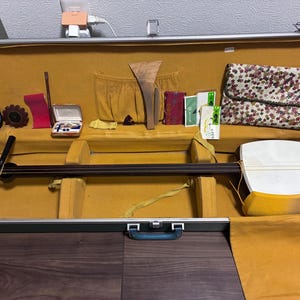 May include: An open green case with a traditional Japanese shamisen, accessories, and a floral patterned pouch. The shamisen has a long neck and a white body with a yellow border. Various tools and accessories are arranged inside the case.