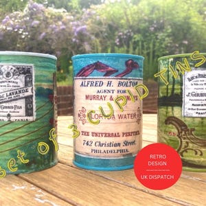 May include: Set of three vintage-style metal tins with colourful labels. The tins feature images of flowers, birds, and a landscape. The text on the labels includes "Eau de Lavande", "Alfred H. Bolton", "Lorida Water", "The Universal Perfume", "742 Christian Street, Philadelphia", and "J. Giraud Fils".