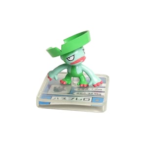 May include: A green and blue figurine of a cartoon character with a large green hat. The figurine is standing on a clear plastic base with Japanese text. The character has a red mouth and is in a playful pose.