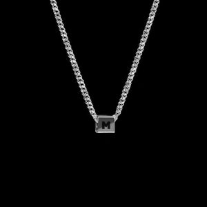 May include: A silver chain necklace with a small silver pendant featuring the letter "M" in black.