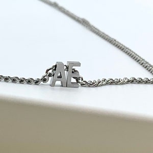 May include: A silver chain necklace with a silver charm that says "AE".