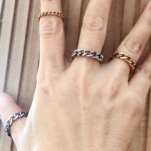 May include: Three chain link rings in gold, silver, and black on a hand.