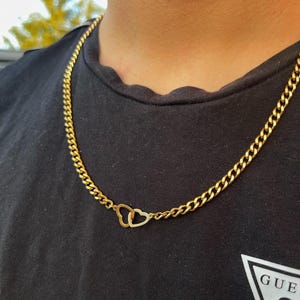 May include: A gold chain necklace with a double heart pendant. The chain is a curb style and the hearts are interlocking.