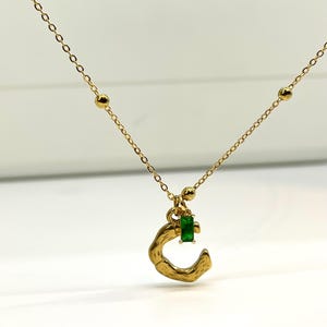 May include: A gold chain necklace with a small green gemstone and a gold letter 'C' pendant.