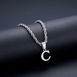 May include: A silver-toned necklace featuring a rope chain and a pendant shaped like the capital letter C. The pendant is attached to the chain by a simple metal bail, and the entire piece has a polished, metallic finish with a smooth surface.
