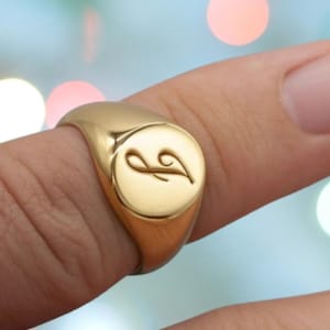 May include: A gold signet ring with a cursive letter "L" engraved on the face.