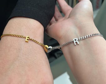 May include: Two matching bracelets with a heart charm connecting them. One bracelet is gold with the letter "E" and the other is silver with the letter "R".