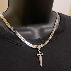 May include: A silver curb chain necklace with a silver sword pendant. The sword has a cross at the top and is detailed with intricate designs.