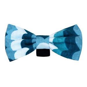 May include: A blue and white bow tie with a geometric pattern. The bow tie is made of fabric and has an adjustable strap.